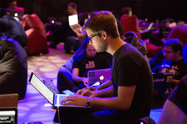 Un groupe d'hommes, qui sont adultes, sont assis à l'intérieur la nuit dans une salle, regardant une représentation sur scène qui intègre la technologie.